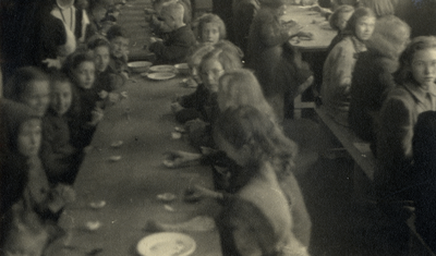 811770 Afbeelding van enkele kinderen tijdens een gezamelijke maaltijd van een gaarkeuken in een lokaal in de omgeving ...